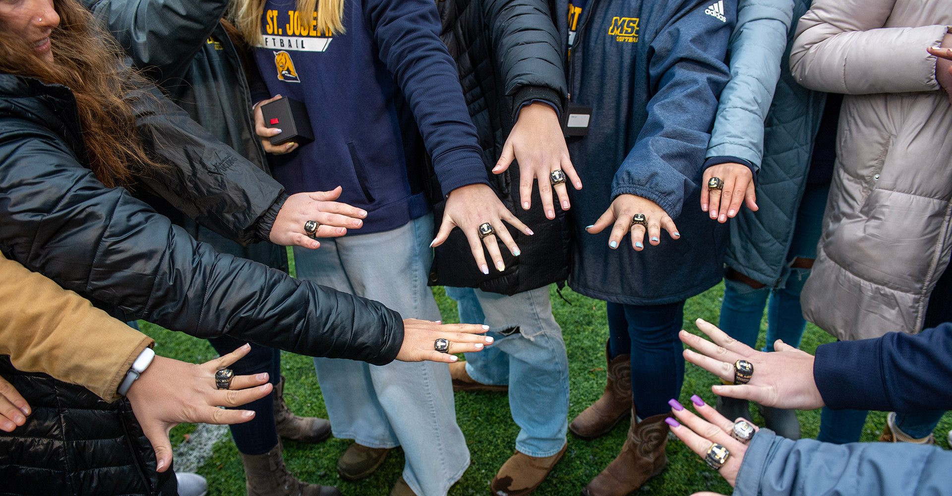 softball players with hands in a group huddle with class rings on