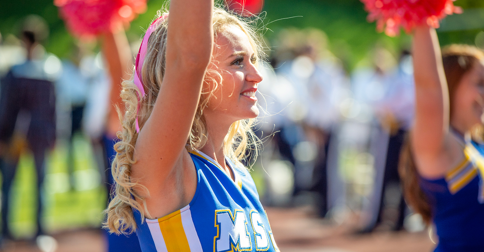 msj cheerleader raising arm with pom-pom and and smiling