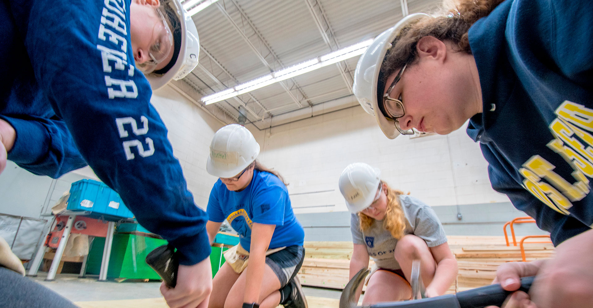 MSJ students in construction hats using hammers.