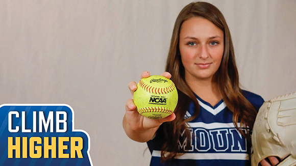 Casey Kemp holding NCAA softball to camera in her MSJ softball uniform with a mitt in hand.