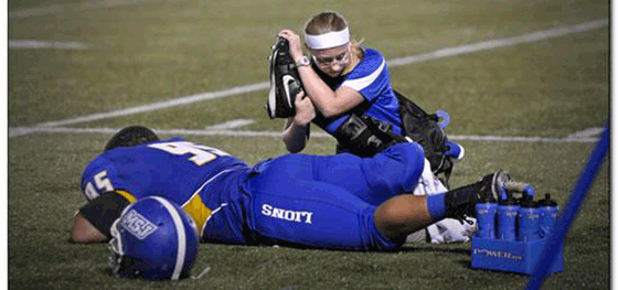 Athletic trainer stretching leg of athlete