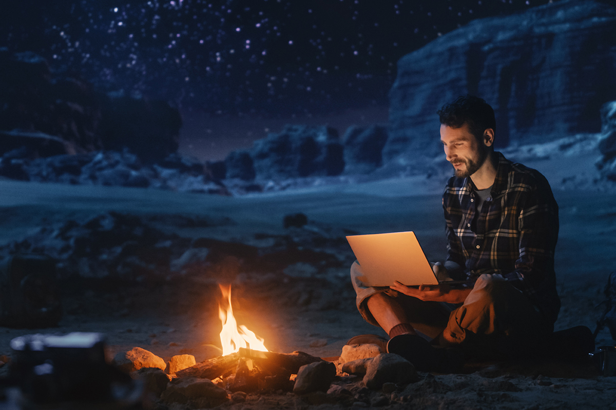 male student on laptop by a campfire.