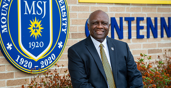 president H. James Williams sitting and smiling outside of the centennial fieldhouse indoor track