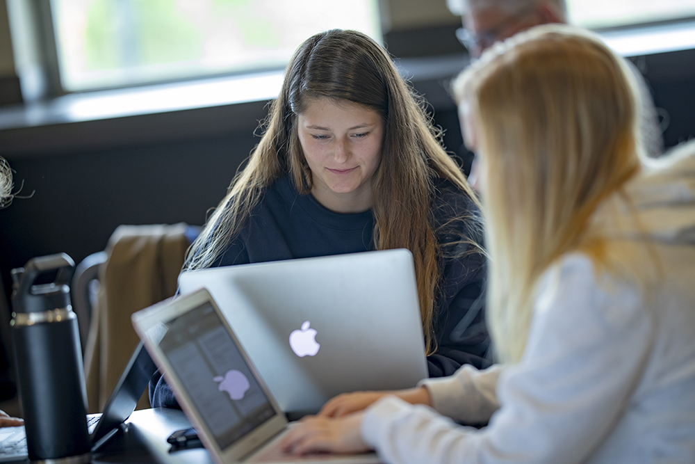 two female students on laptops at table.