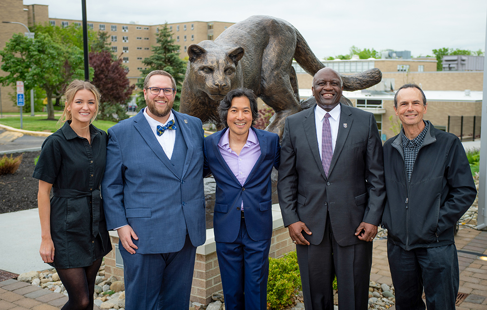 Group of people who brought the Catamount to creation standing smiling in front of the Lion Sculpture at Mount St. Joseph University