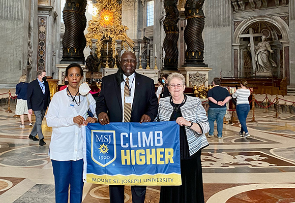 president williams, mrs. carole williams, and sister karen elliott holding climb higher banner in vatican in Rome.