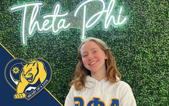 alyssa baker smiling by theta phi alpha sign on wall