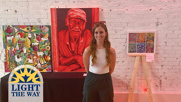 woman stands with paintings behind her