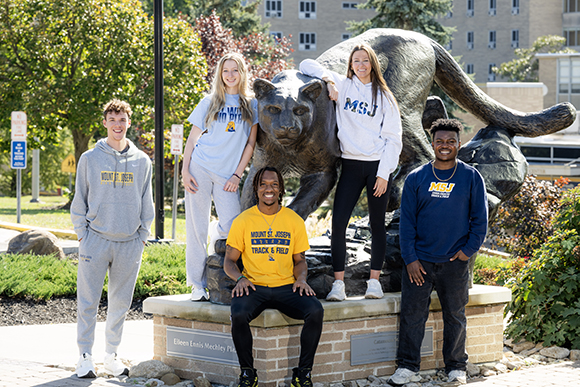 students standing next to lion sculpture outside